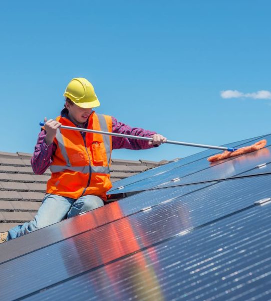 young worker cleaning solar panels on house roof