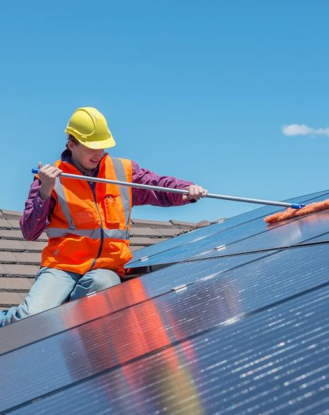 young worker cleaning solar panels on house roof